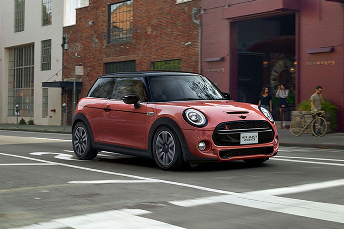 The MINI COOPER HARDTOP CORAL RED EDITION driving in the city.