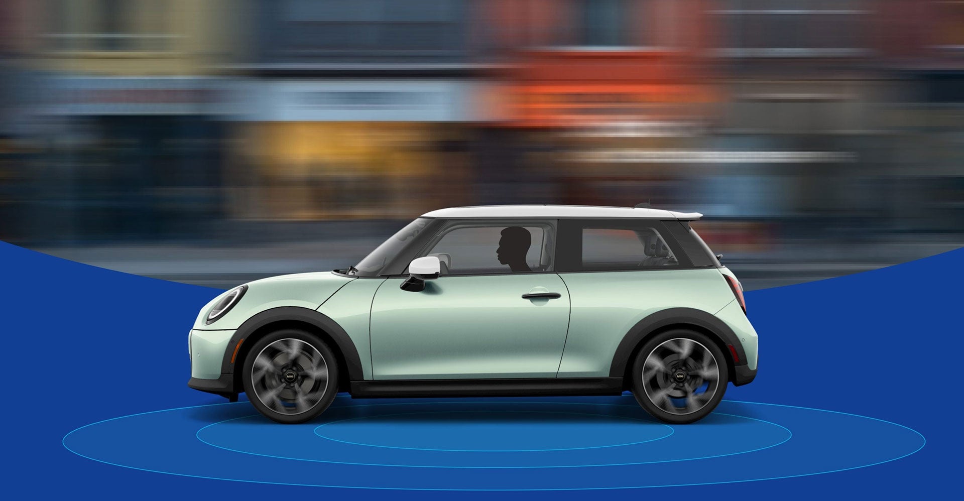 The side-view of a Mini Cooper Hardtop 2 Door with a blurred city street in the background and blue rings beneath it.