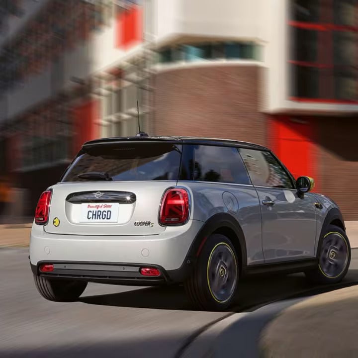 Three-quarters back view of a MINI Electric vehicle rounding a street corner in an urban setting with its surroundings blurred out.